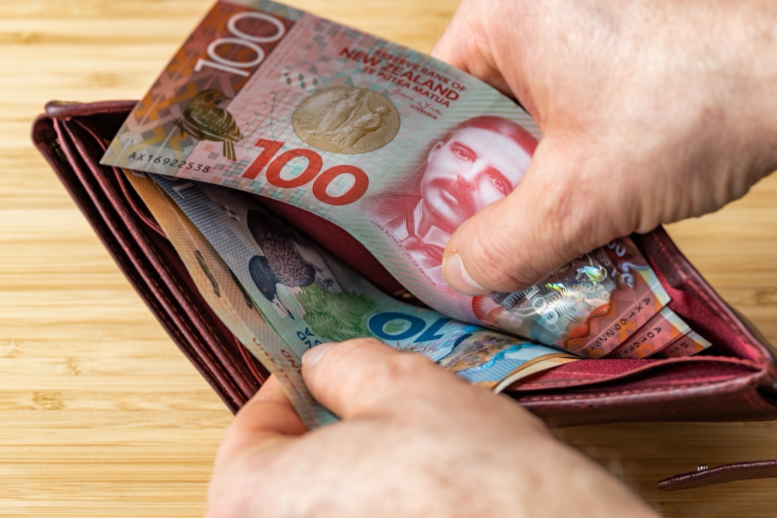 Hand placing New Zealand $100 banknote into a leather wallet
